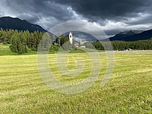 Stormy sky over a green clearing near the Church of San Gian in Celerina, Switzerland