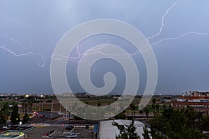 Stormy sky with several huge lightnings bolts on the outskirts of a city over agricultural fields