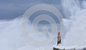 Stormy wave over old lighthouse and pier of Viavelez.