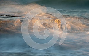 Stormy windy sea waves splashing on a rocky seashore at sunset