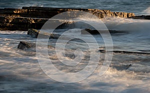 Stormy windy sea waves splashing on a rocky seashore at sunset