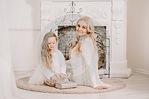 Story Time with Mother and Daughter in Front of Fireplace. Pretty family with book. Mom and child sitting close and