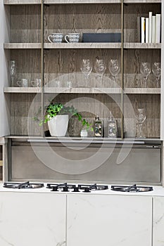Stove closeup in modern kitchen interior. Gas burners built into the countertop. Hanging glass shelves with glasses