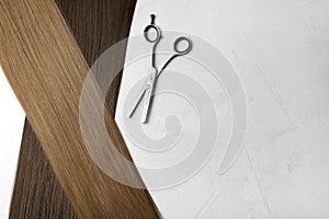 Straight brown hair and thinning scissors on light background, flat lay