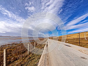 Straight country road among mountains and lake with beautiful cloudy sky background in gahai National Nature Reserve park