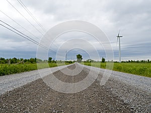 Straight gravel road landscape with a wind turbine and power lines