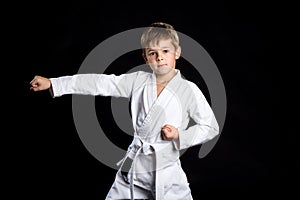 Straight karate arm hit. Kid in brand new kimono looking on the camera on black background