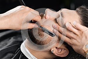 Straight razor cut mans beard in barbershop. Barber man making hairstyle for handsome man.