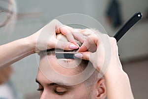 Straight razor. haircut process of blond young man in barbershop salon