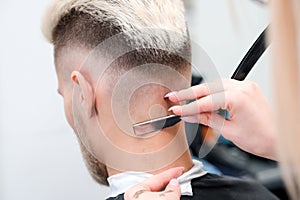 Straight razor. haircut process of blond young man in barbershop salon