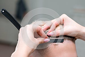 Straight razor. haircut process of blond young man in barbershop salon