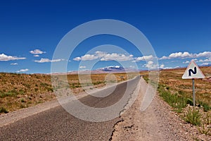 Straight road in desert with blue sky and a traffic sign