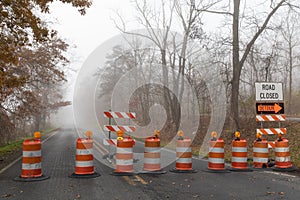 Straight road disappearing into a dense fog, barricade of bright orange traffic barrels