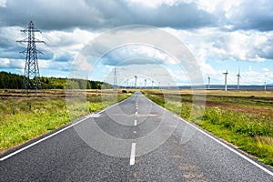 Straight road to wind turbine and cloudy sky