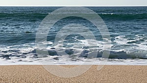 Straight on view of waves breaking on the shore of a sandy beach in spring time in Portugal.