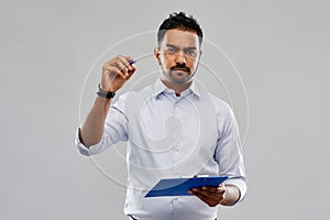 Strained indian businessman writing to clipboard