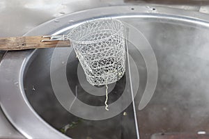 Strainer basket for blanching noodles laying over a pot.