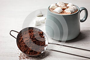 Strainer with cocoa powder and cup of hot drink on wooden table