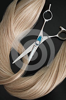 A strand of blond hair with scissors on a black background. Close-up.