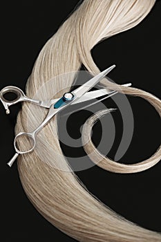 A strand of blond hair with scissors on a black background. Close-up.