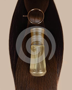 A strand of natural dark hair for extensions with a bottle of care product.