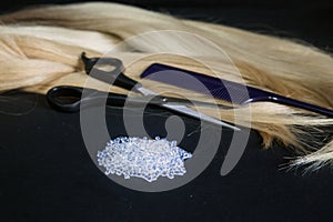 strands of hair extensions with a pair of scissors and white keratin on black background