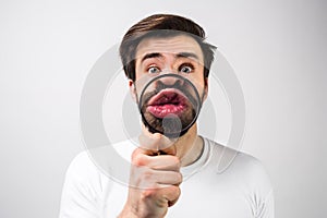 Strange and amazed man on white background and making some fun with putting a loupe in front of his mouth. Guy