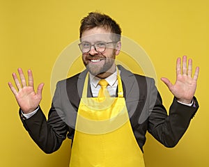 Strange, charming business man in a black suit and yellow apron, made a good deal, he rejoices, smiles and raises palms