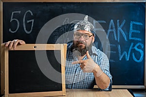 A strange guy conspiracy theorist in a protective aluminum foil hat and glasses sits at a table and points his finger at
