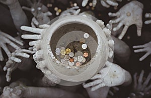 Strange hands hold a pot of coins. Chiang Rai, white temple. Thailand