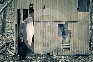 A strange hooded figure with a white sheet covering his face. Standing next to an abandoned forest hut in winter