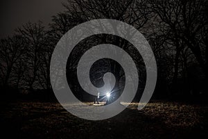 strange light in a dark forest at night. Silhouette of person standing in the dark forest with light. Dark night in forest at fog