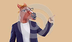 Strange man in a suit, a funny horse mask and glasses pointing his finger to the side