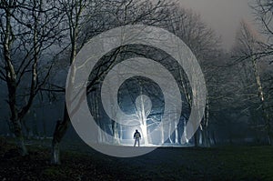 Strange silhouette in a dark spooky forest at night, mystical landscape surreal lights with creepy man