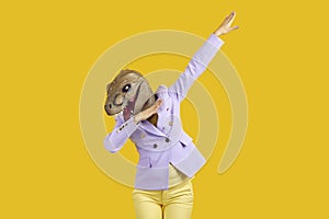 Strange woman in funny dinosaur mask doing dab move isolated on yellow background