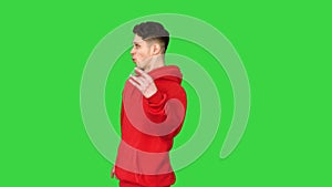 Strange young man in red hoody walking backwards on a Green Screen, Chroma Key.