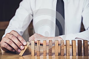 Strategy and successful intervention concept for business, businessman hand Stopping Falling wooden Dominoes effect from