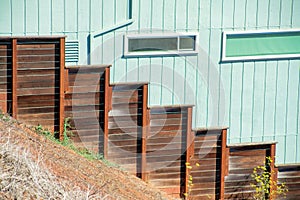 Stratified fence going down hill made or dark stained wood with natural hill foreground and wooden green suburban house