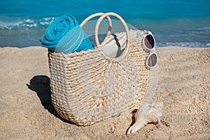 Straw bag with blue towel and sunglasses on tropical sand beach