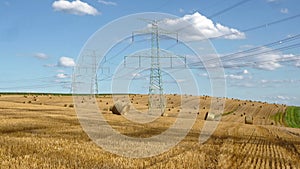 Straw bales on the field near high electricity pylons
