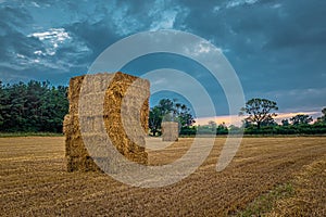 Straw bales stacked in a field under a threatening sky.