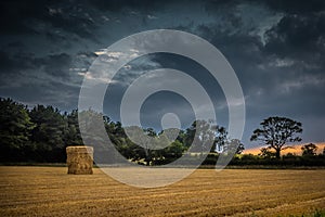 Straw bales stacked in a field under a threatening sky.