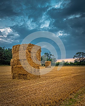 Straw bales stacked in a field under a threatening sky.