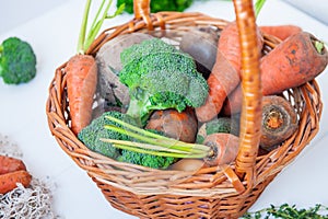 Straw Basket with garden Vegetables - fresh carrots, beets, broccoli, onions on the white wooden background. Farm Harvest. Food or