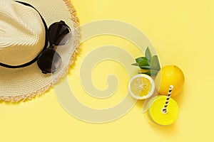 Straw beach foman`s hat and black sun glasses with citrics water on yellow. Top view. Flat lay.