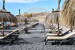 Straw beach umbrella with blue sky, sunbeds on the black volcanic beach of La Caletta. Tenerife, Canary Islands, Spain