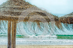 Straw Beach Umbrellas on Sand Beach Turquoise Sea Waves Blue Sky Background. Bright Sunlight. Summer Vacation Wanderlust Traveling