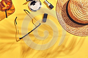 Straw beach woman`s hat, beverage with ice in a glass and sun glasses on yellow background with shadow from a palm leaf.