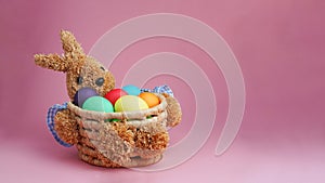 Straw bunny basket with easter colorful eggs on pink background. Happy Easter. Copy space. Close up