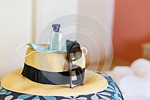 A straw hat on a bag with a mask, hand sanitiser and sunglasses.